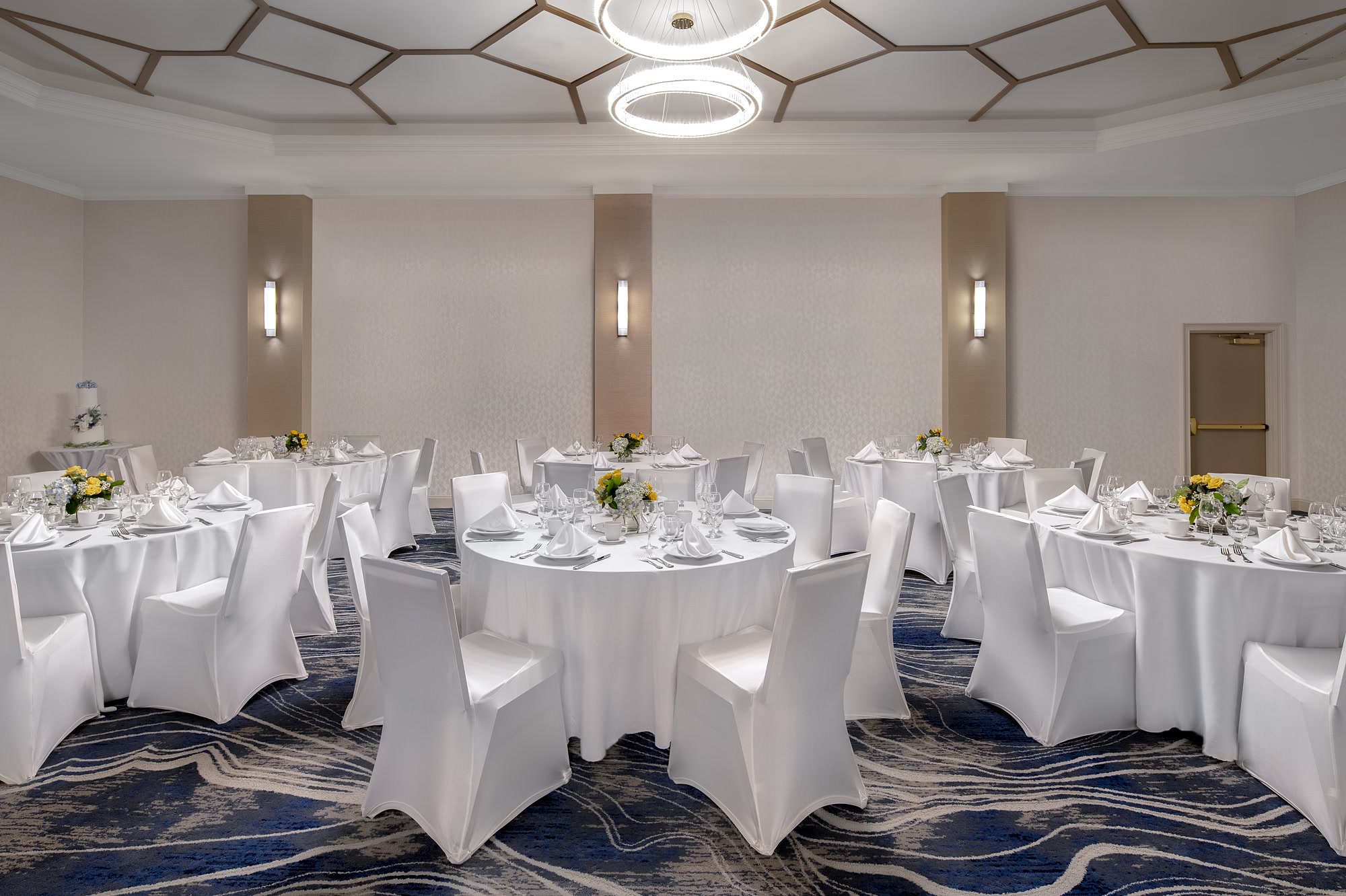 The Grand Ballroom set with white linen rounds and a cake beneath the ring chandeliers